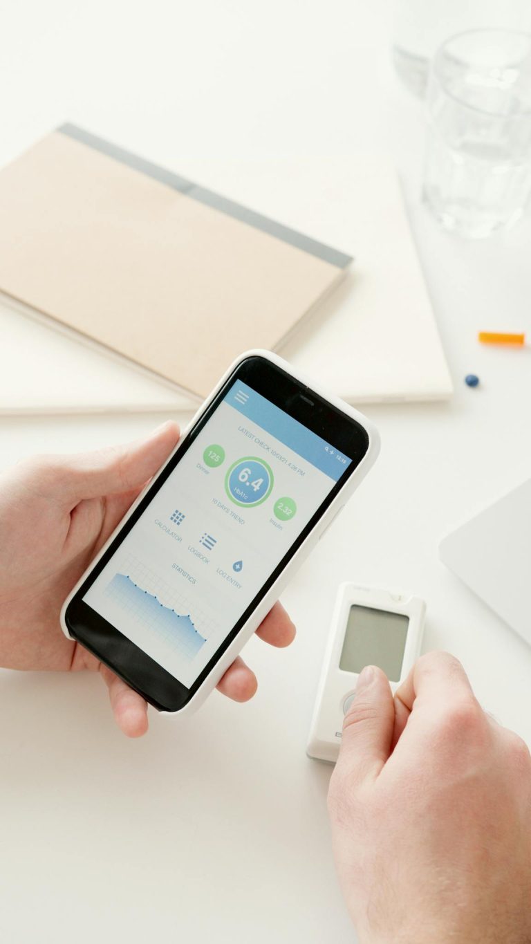 Close-up of hands using a smartphone app to monitor glucose levels with a digital glucometer on a table.
