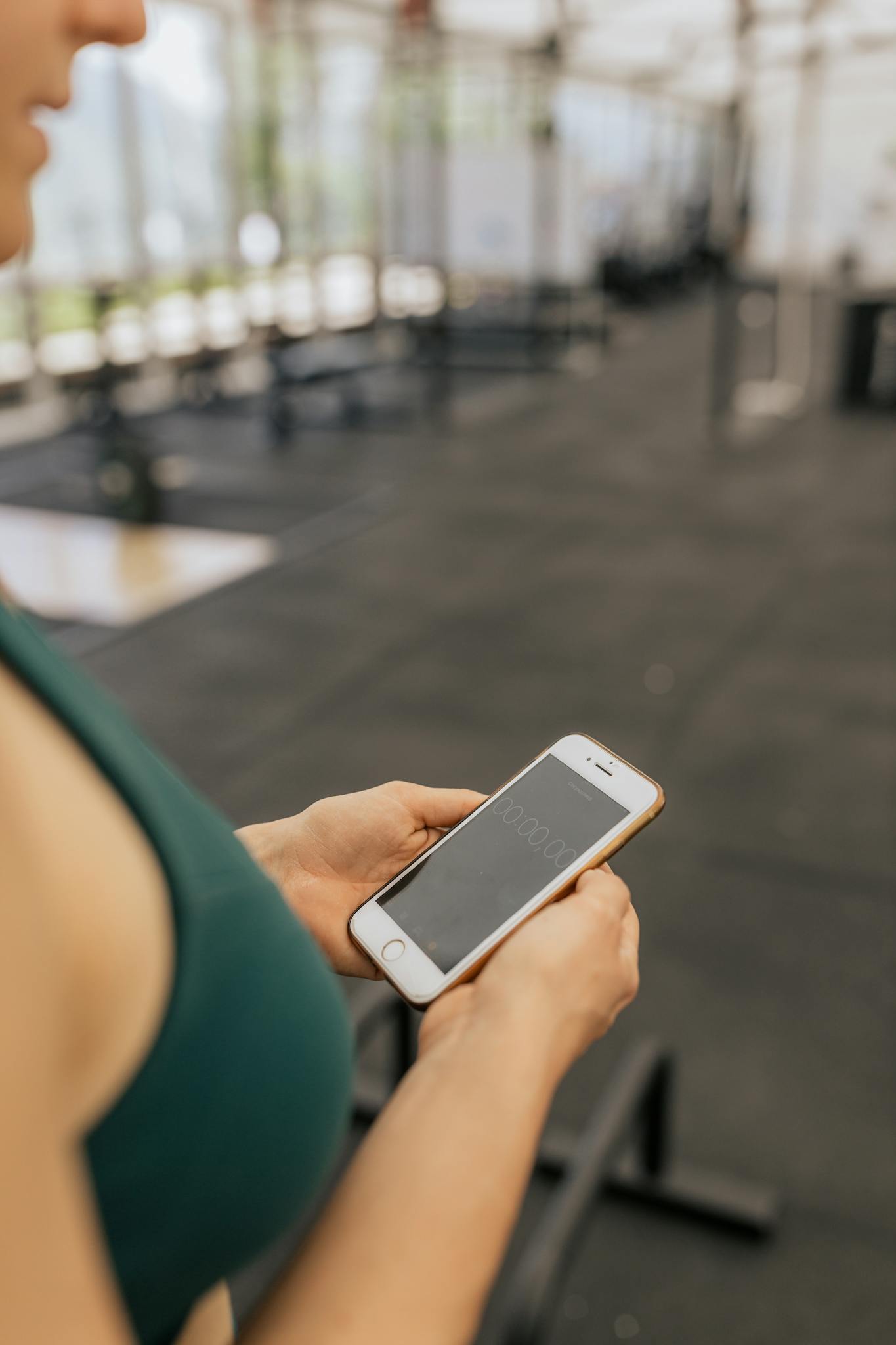 Woman checks timer on smartphone while working out in gym.